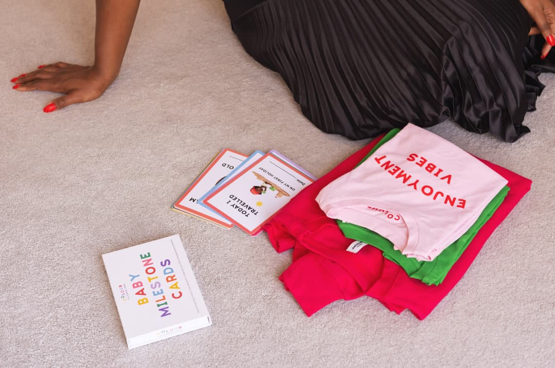 Two of the Colourful Celebrations products are shown on a carpet: t-shirts and baby milestone cards