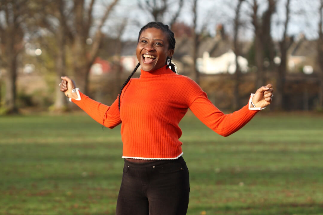 Woman in orange jumper smiling in a park
