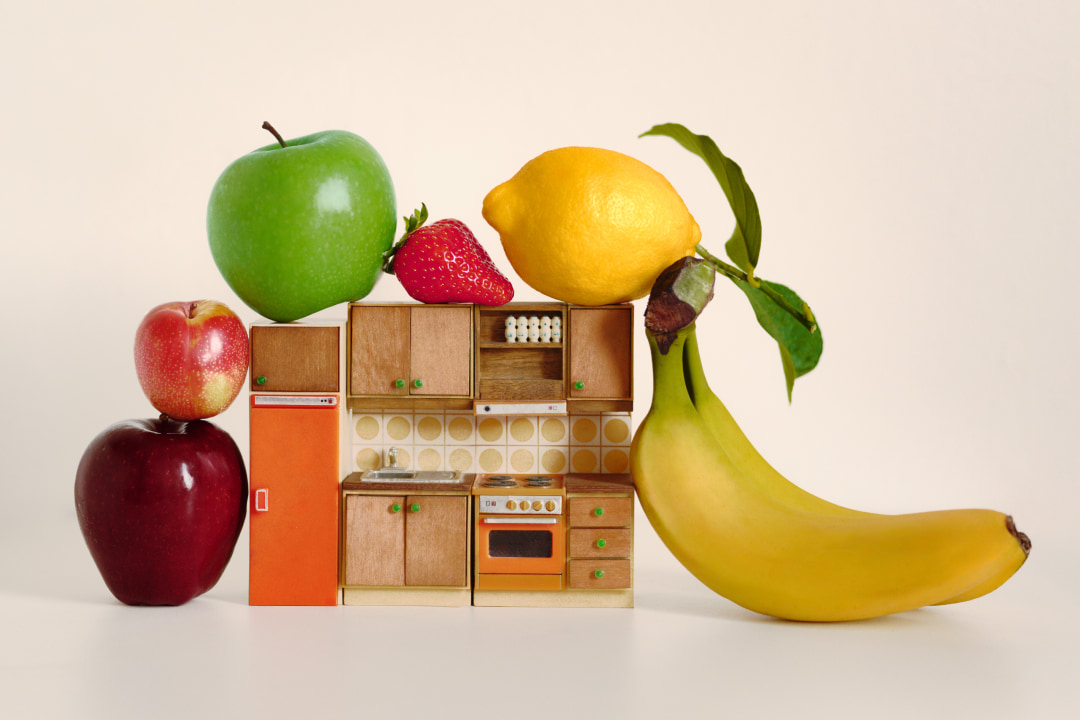 Creative photograph of a doll's house sized kitchen set surrounded by fruit
