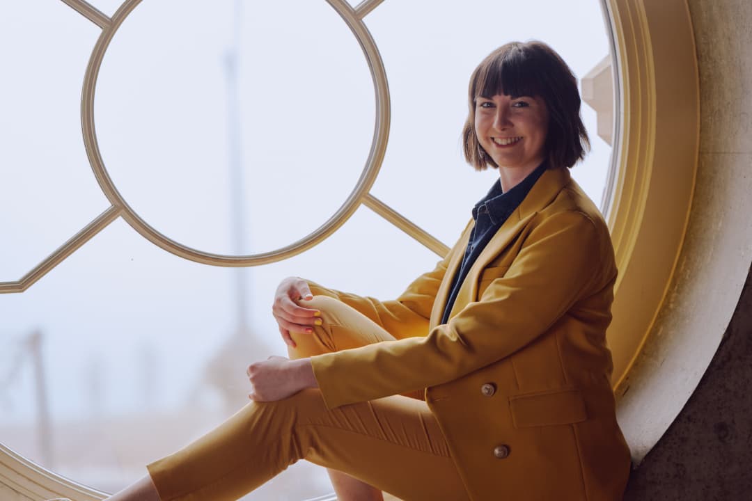 Pippa Moyle, founder of City Girl Network, dressed in a yellow suit by a round window.
