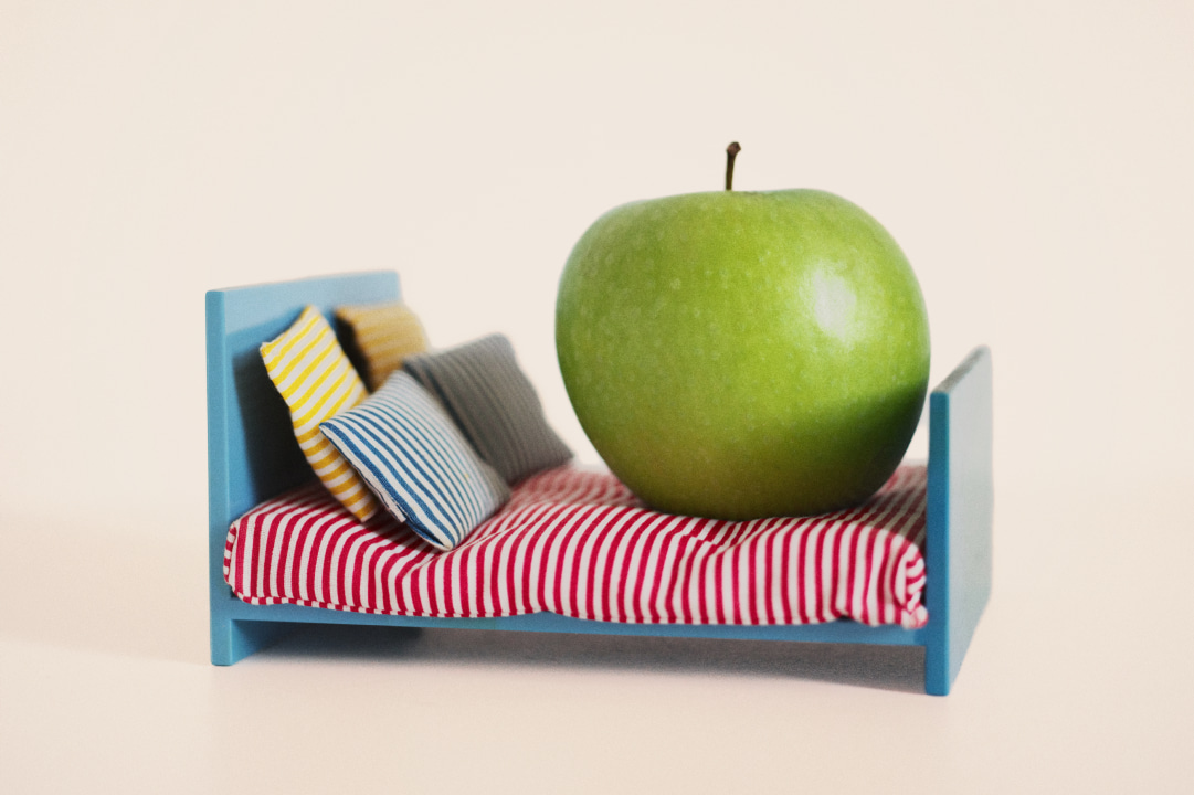Creative photograph of a green apple on top of a doll's house sized wooden bed