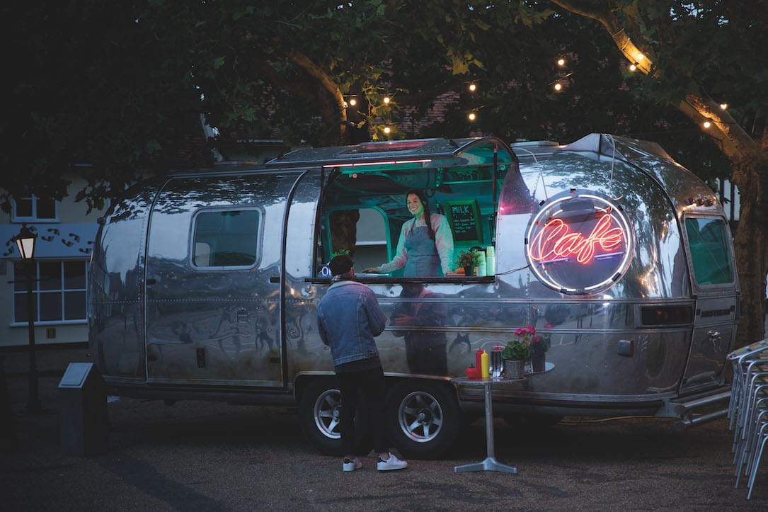 A woman stands inside of her teal lit coffee truck.