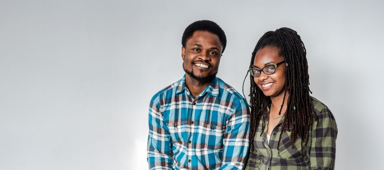 A man wearing a blue checked shirt and a woman with glasses wearing a green checked shirt sitting down