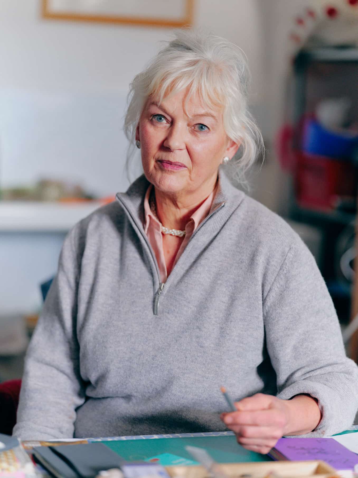 Sculptor Deirdre Nicholls looking to camera in her studio. She is wearing a pink shirt and grey jumper.