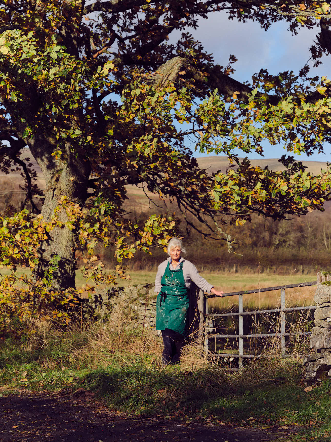 Sculptor Deirdre Nicholls standing outside next to an oak tree with fields in the background