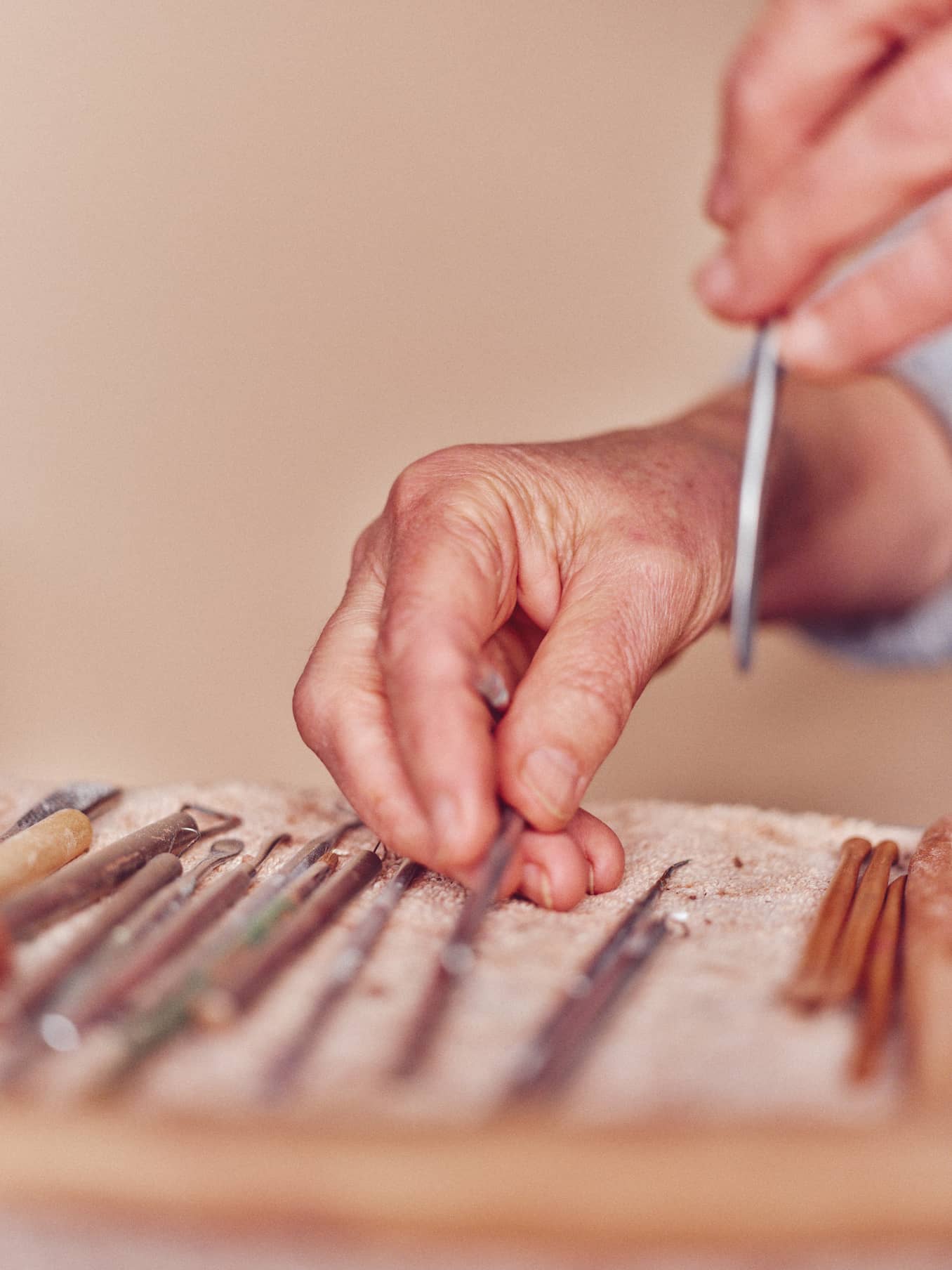 Photograph of hands arranging a selection of sculpture tools with a muted background