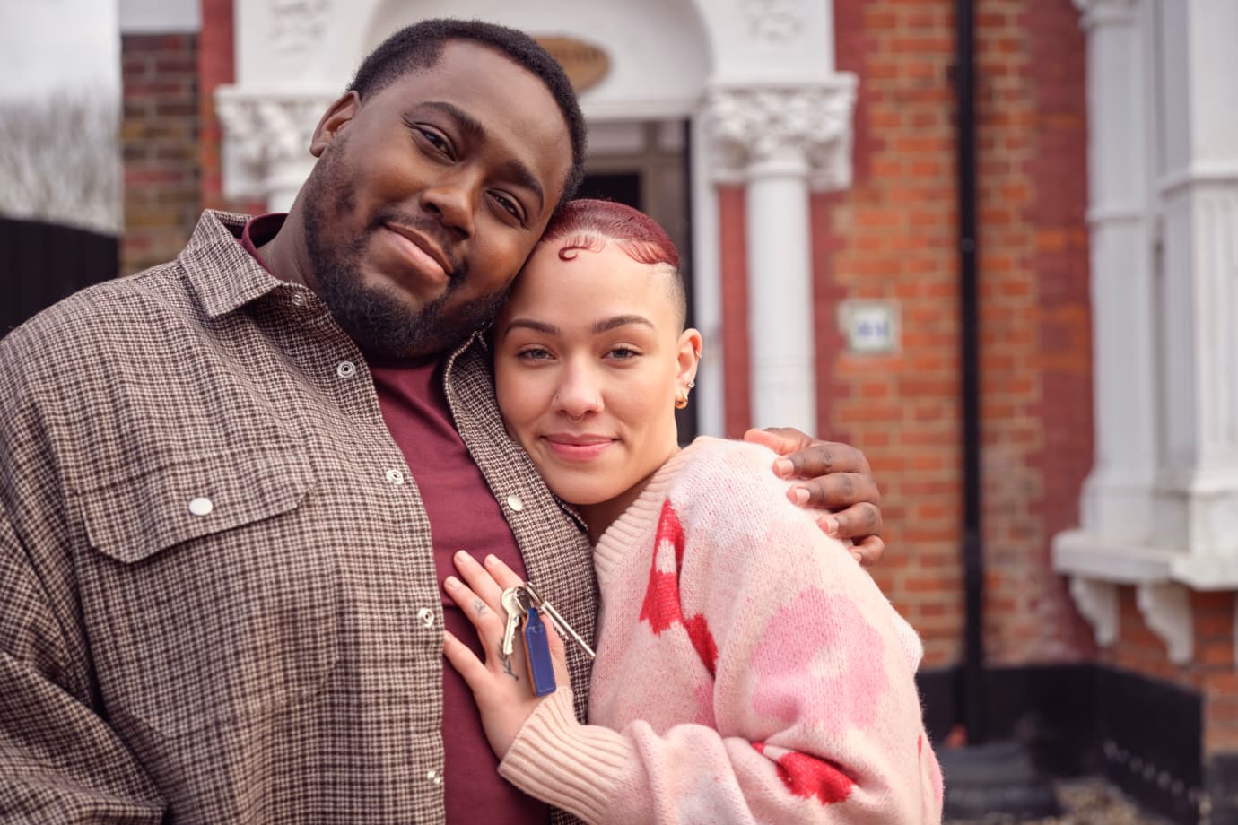 A couple standing outside a house, holding keys.