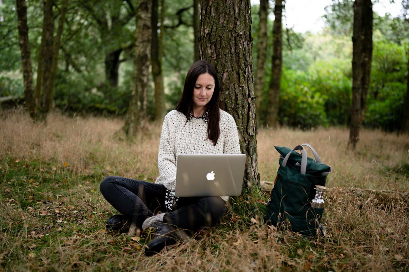 Charlotte is sitting with a laptop near the tree