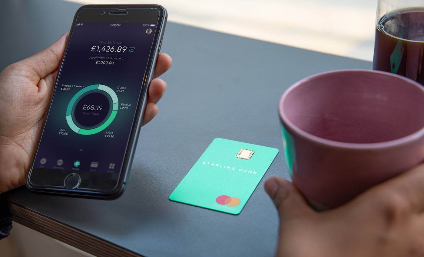 A person holding a coffee and a mobile phone, with the account balance screen displayed on their app