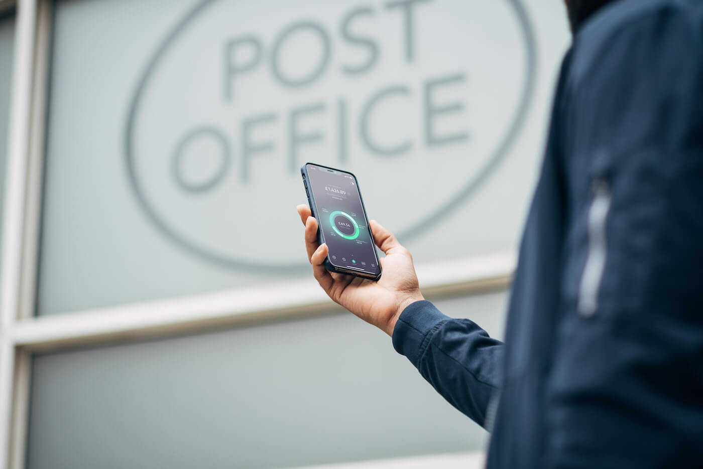 A phone in a hands with the Post Office on the background