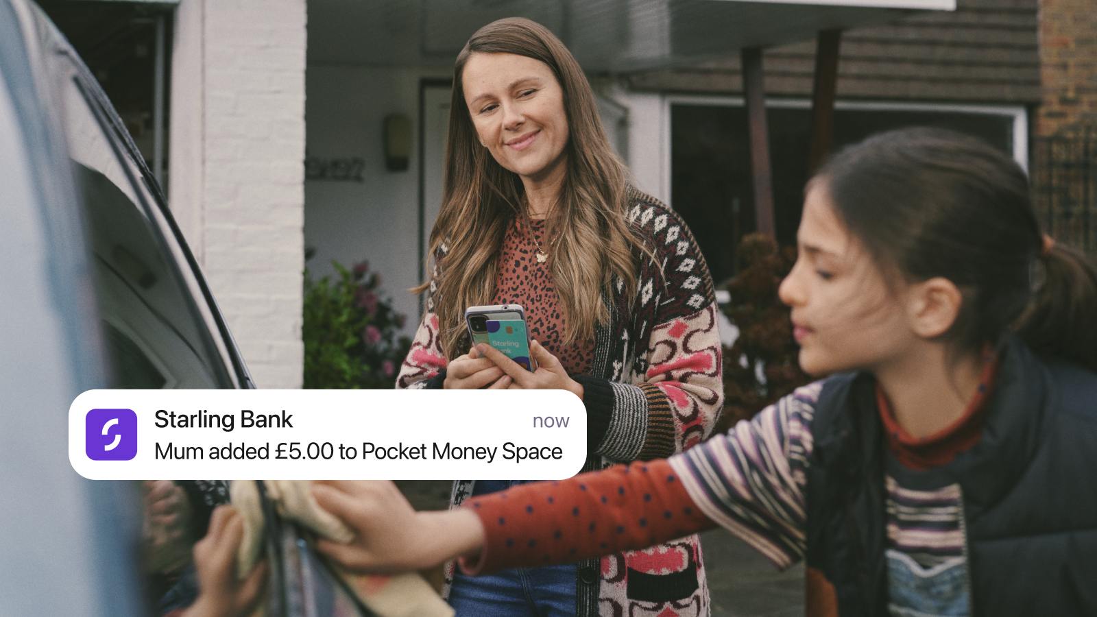 A woman holds a phone and stands next to a child. Notification on a screen from Starling Bank: "Mum added £5.00 to Pocket Money Space