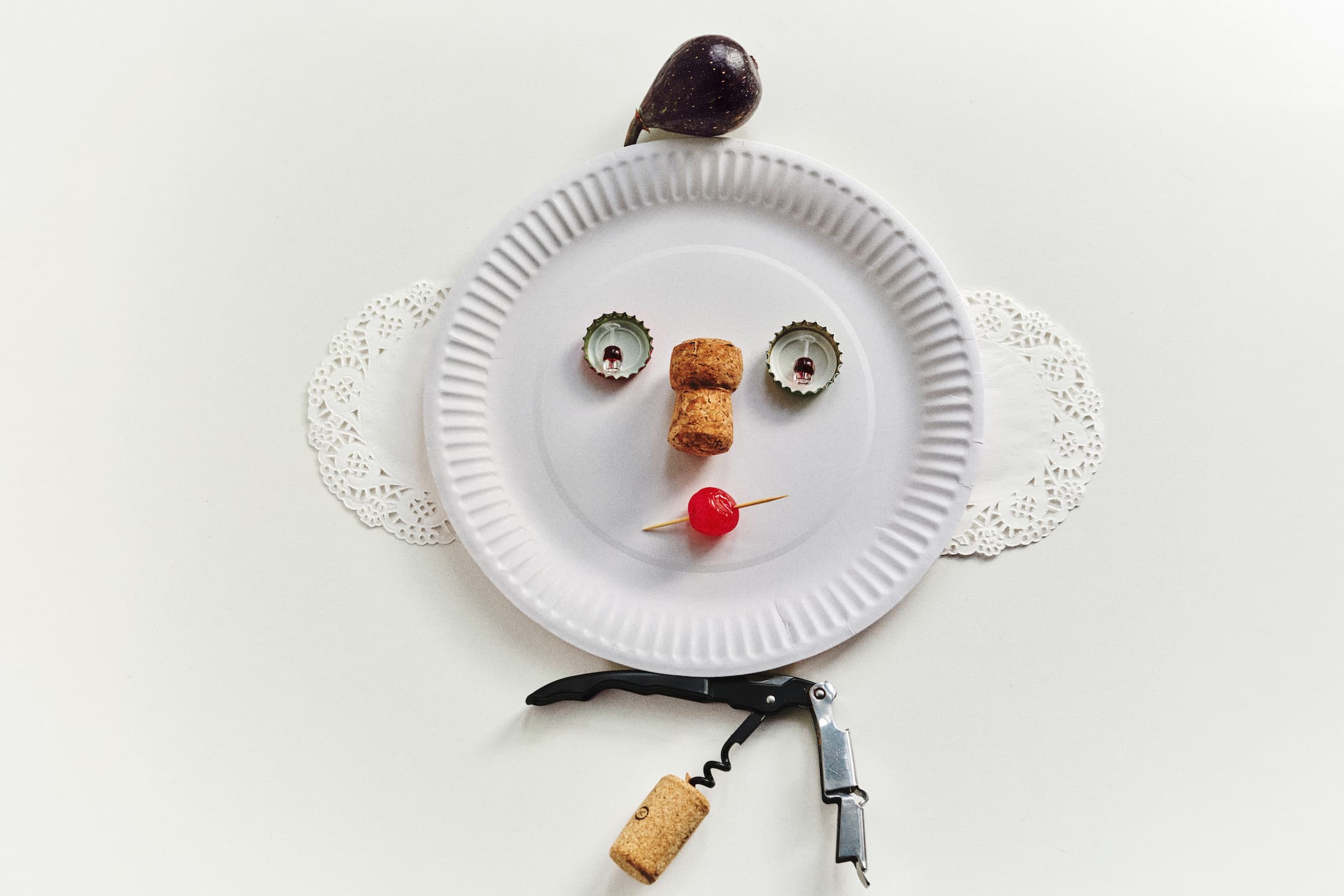 A makeshift face using bottle caps, a cork and a maraschino cherry
