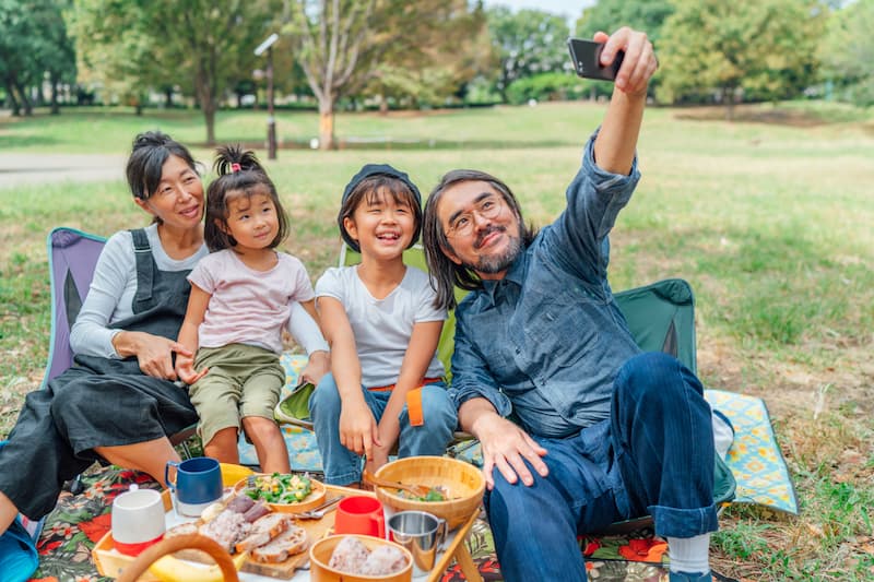 A family having a picnic on a field, taking a photo on a mobile phone