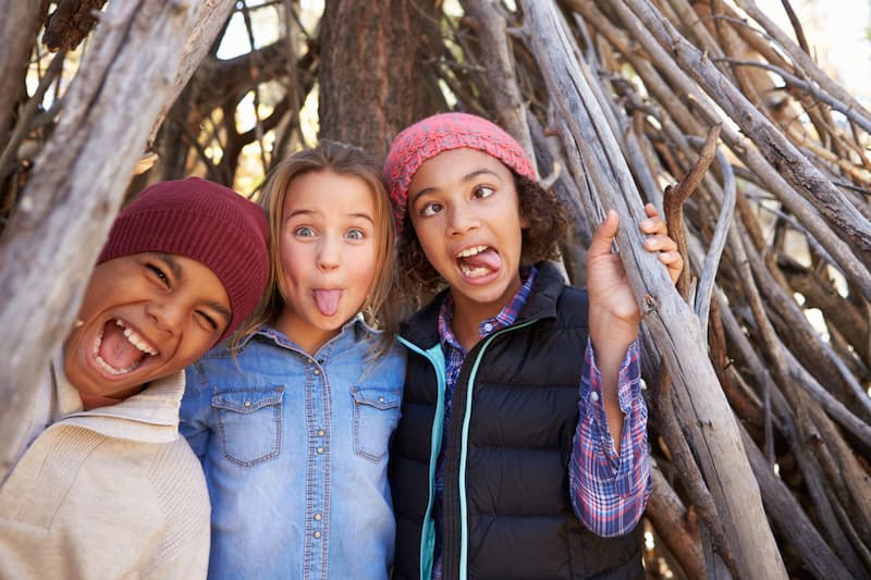 Three children having fun in a den made of tree branches
