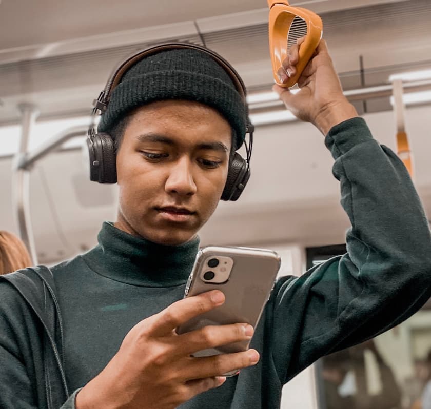 Young man on the subway wearing headphones staring at his phone