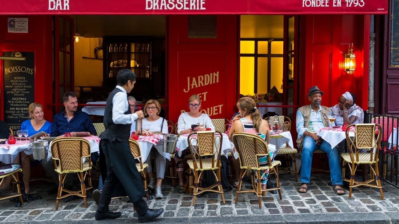 People sitting outside a brasserie withe a waiter holding a bottle